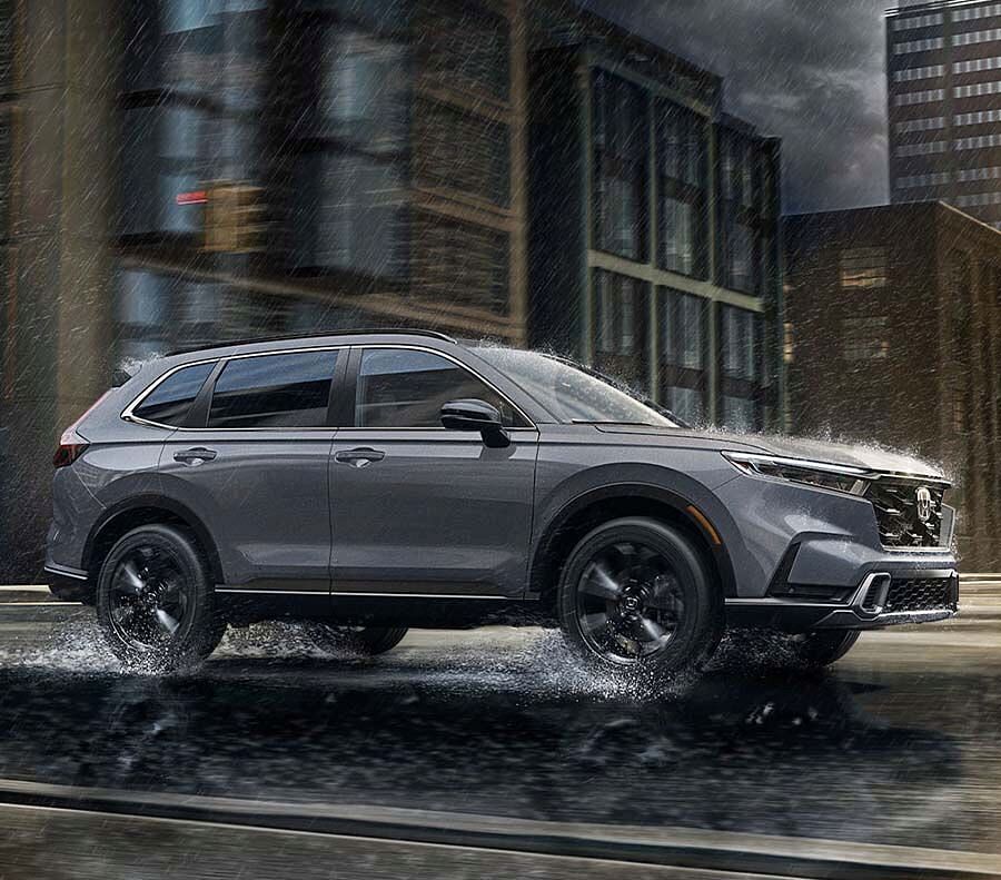 Side shot of silver 2024 Honda CR-V driving on rainy street.
