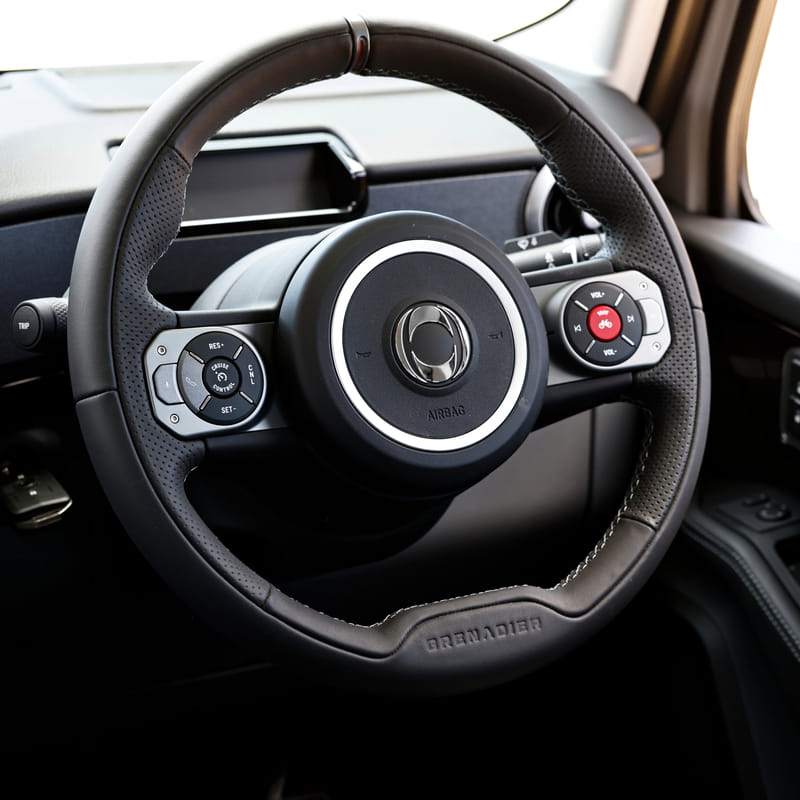 Close-up of a modern car steering wheel, featuring integrated controls on both sides, and sleek black leather design. Airbag text is visible.