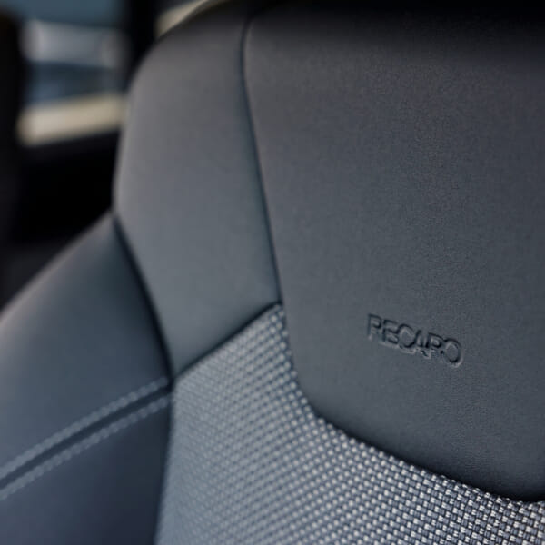 Close-up of a car seat headrest featuring the 'RECARO' logo, showcased with sleek black leather and textured fabric, conveying luxury and comfort.