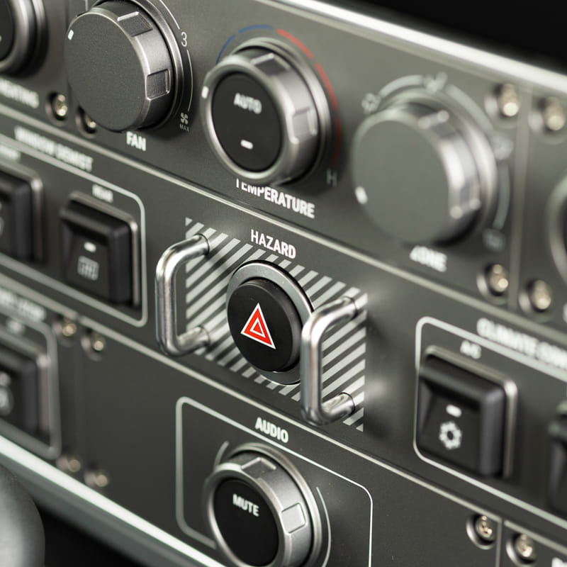 Close-up of a car dashboard featuring various controls, including a rubberized hazard button with a triangle symbol, conveying precision engineering.