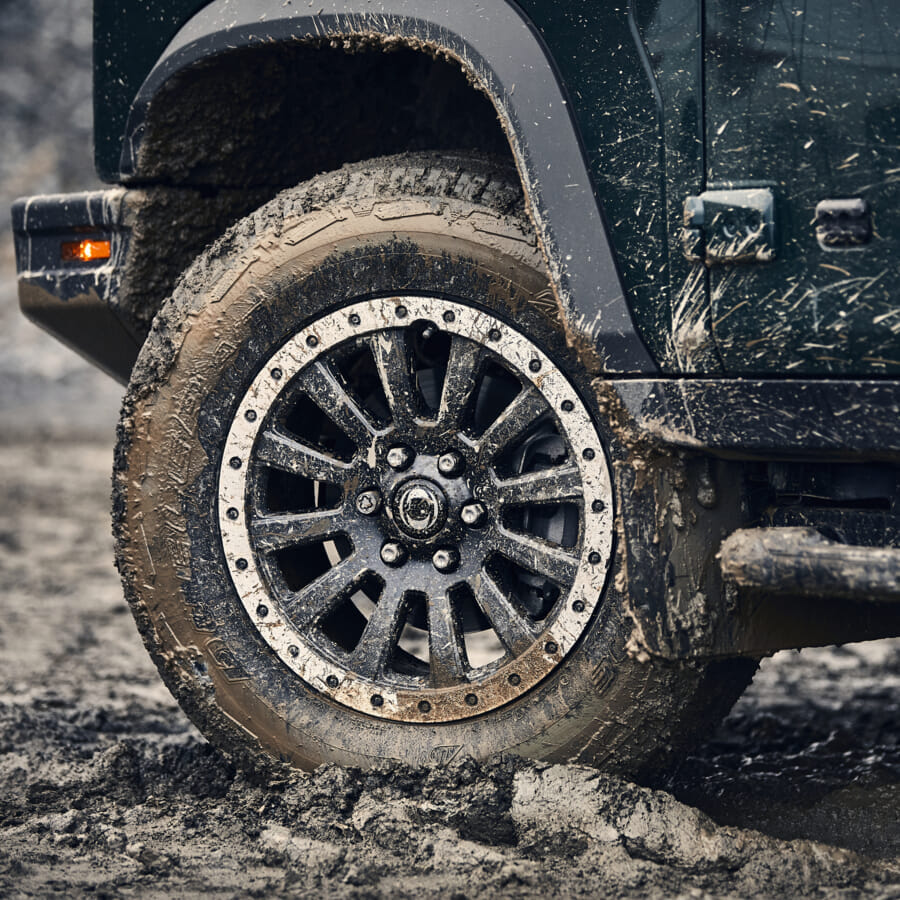 Close-up of a Jeep's front tire caked in mud, highlighting rugged off-road capability. The vehicle is dark green, conveying a sense of adventure.