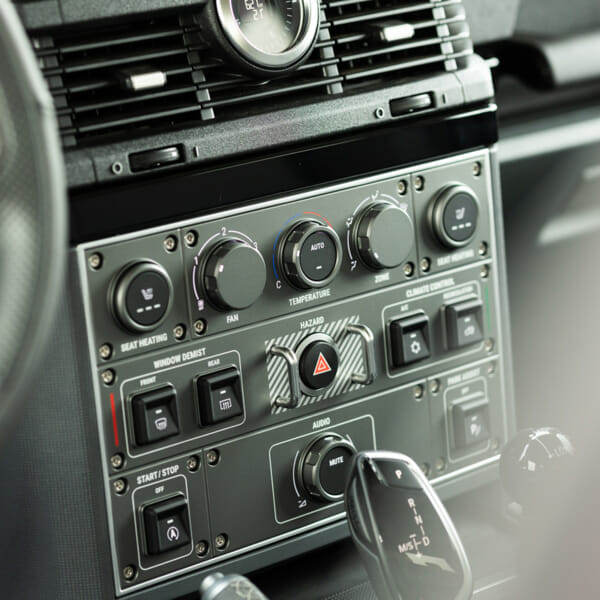 Close-up of a car dashboard with controls for fan, temperature, and climate. Features buttons for seat heating, window demist, and hazard lights.
