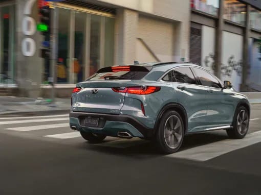 A sleek silver SUV driving through a city street. The vehicle's modern design and clear lines are highlighted under urban buildings and signals.