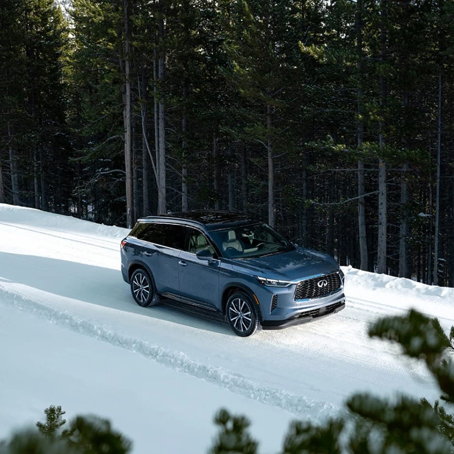 A blue SUV drives along a snowy, forested road, flanked by tall pine trees, conveying a sense of adventure and winter tranquility.
