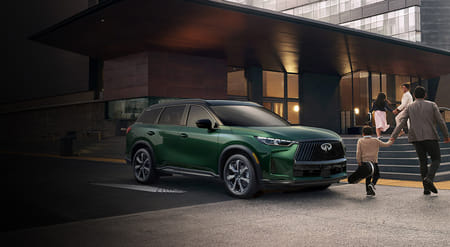 Man and child holding hands while walking in front of parked 2026 QX60.
