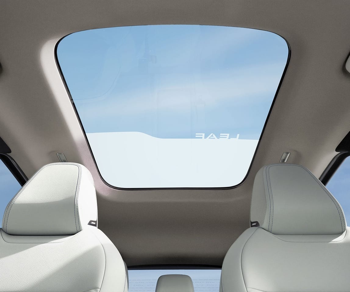 View of a panoramic sunroof from inside the 2026 Nissan Leaf, showing two light-colored front seats and a clear blue sky through the glass.