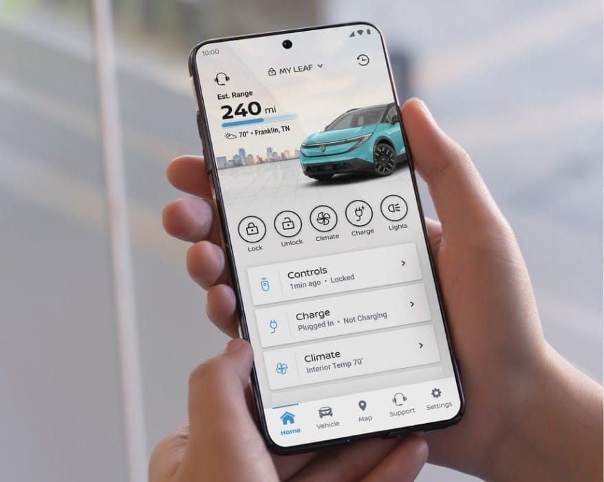 Person holding a smartphone displaying a car control app for a blue electric vehicle with 240-mile range. Features include lock, climate, and charge status.