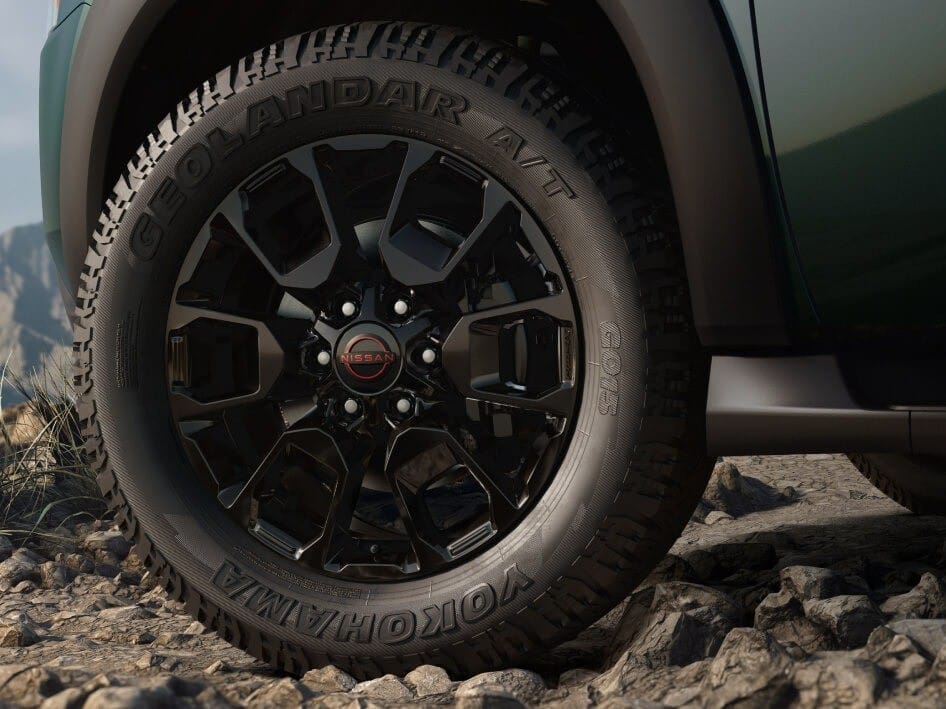 Close-up of a black alloy wheel on a 2026 Nissan Armada, showcasing a Yokohama Geolandar A/T tire on rocky terrain.