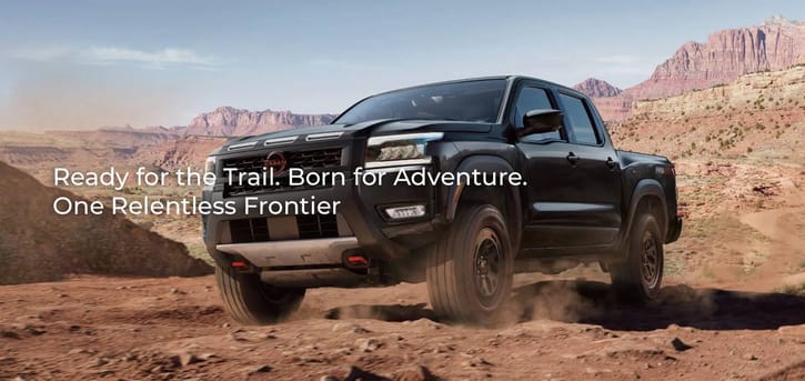 A black 2026 Nissan Frontier PRO-4X conquers a rocky, off-road trail in a desert canyon, showcasing its rugged design and 4x4 capability.
