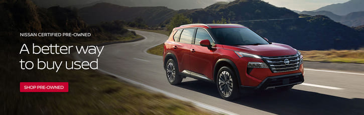 Red SUV driving on a scenic winding road with mountains in the background. Text reads "A better way to buy used" and "Shop pre-owned." Toned for adventure.