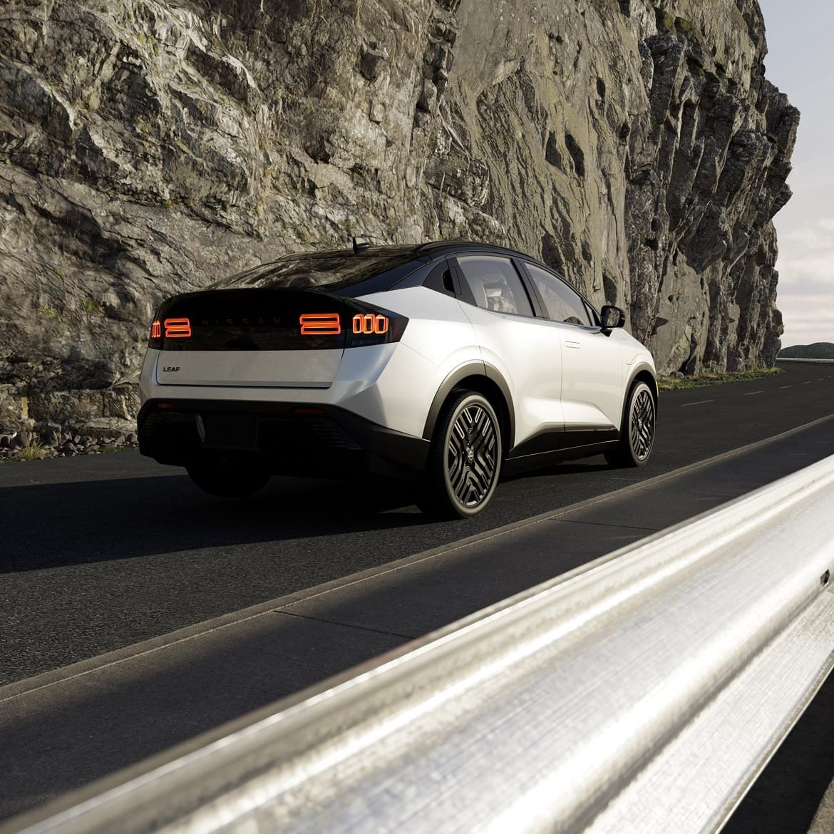 A sleek white Nissan Leaf parked on a winding road alongside a rocky cliff, with a shiny guardrail in the foreground.