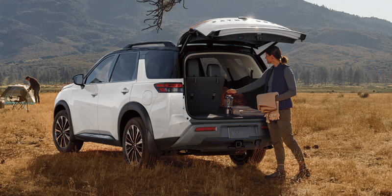 2026 Nissan Pathfinder parked in a field with the liftgate open as the driver unloads gear from the cargo area.