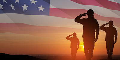 Military men saluting with american flag in the background