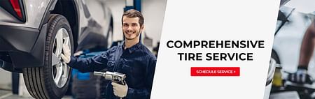 A mechanic holding a tire drill with a car holstered on a lift - COMPREHENSIVE TIRE SERVICE