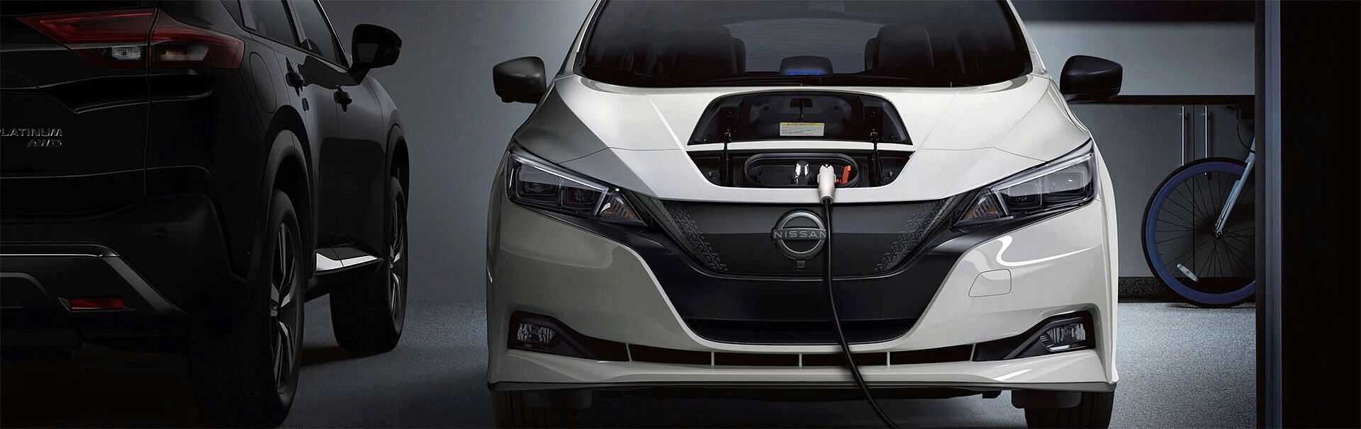 A white Nissan Leaf EV parked with charging port plugged in.