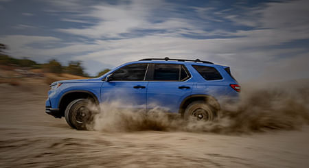 Sideview of light blue 2025 Pilot driving on a desert plain kicking up dust.