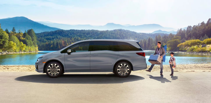Sideview of silver 2026 Odyssey parked lakeside with dad and kid loading up the trunk.