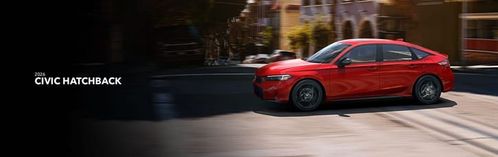 A red 2026 Honda Civic Hatchback speeds down a sunlit urban street, showcasing sleek design and dynamic motion. Bold, modern architecture blurs in the background.