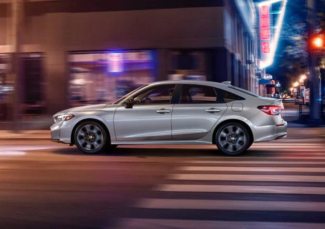 Rallye Red 2025 Honda Civic Hybrid in profile, highlighting its sculpted roofline and available 18-inch alloy wheels.
