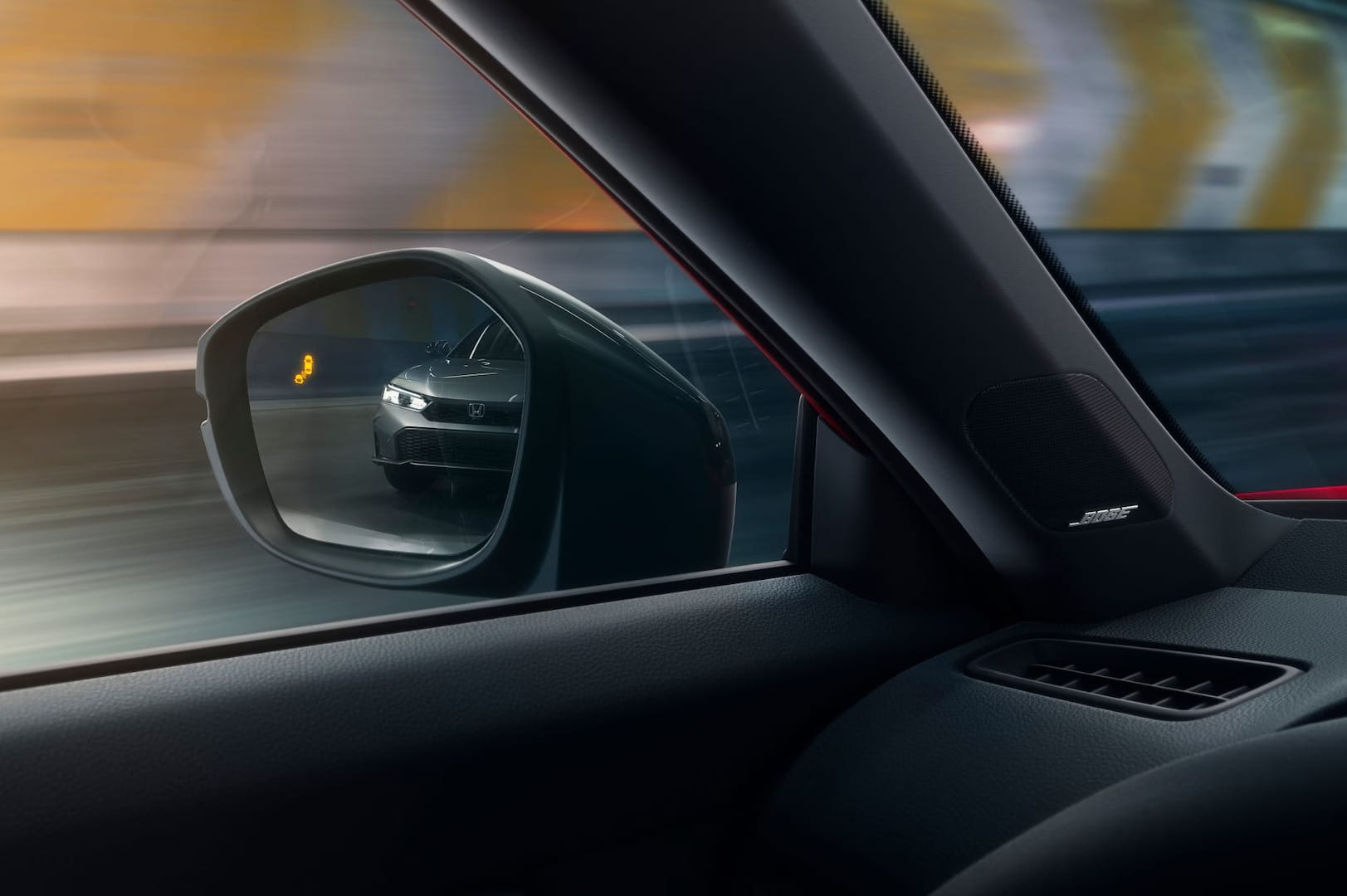 Interior of a moving 2026 Honda Civic Sedan Hybrid showing the side mirror, with a vehicle visible behind. The yellow Blind Spot indicator is visible.