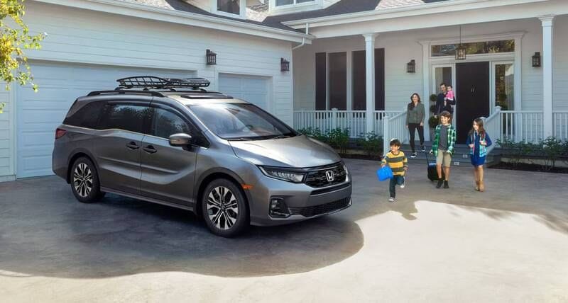 The 2026 Honda Odyssey Elite in Modern Steel Metallic with accessories parked in front of a house with family walking to the vehicle