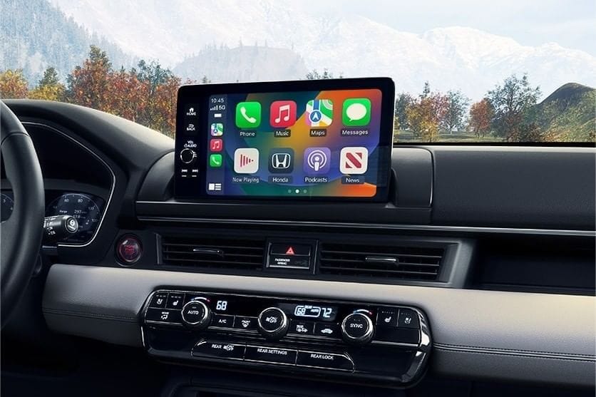 2025 Honda Pilot interior featuring a digital touchscreen display with app icons for music, navigation, and messaging, against a scenic backdrop.