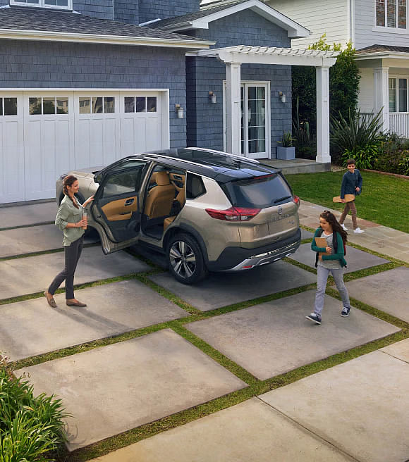 mom opening silver Nissan Rogue door for child in front of a house