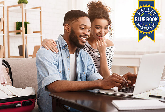 A smiling woman embraces a man typing on a laptop