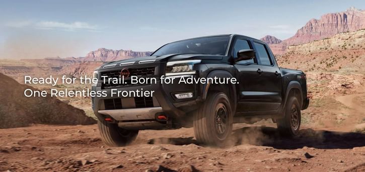 A black 2026 Nissan Frontier PRO-4X conquers a rocky, off-road trail in a desert canyon, showcasing its rugged design and 4x4 capability.
