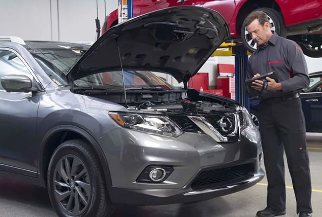 A service technician standing by gray nissan checking checklist