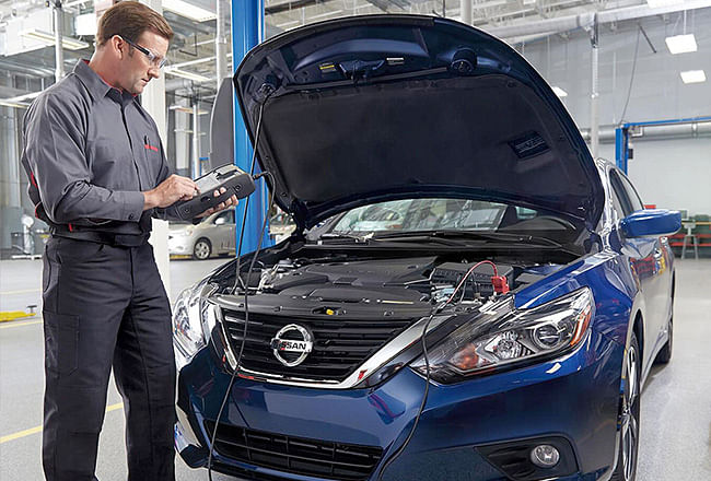 A service technician checking the battery of a blue nissan