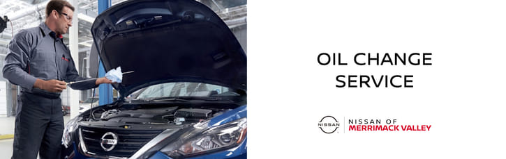 Un banner de servicio de cambio de aceite en Nissan of Merrimack Valley con un mecánico revisando el nivel de aceite de un auto.
