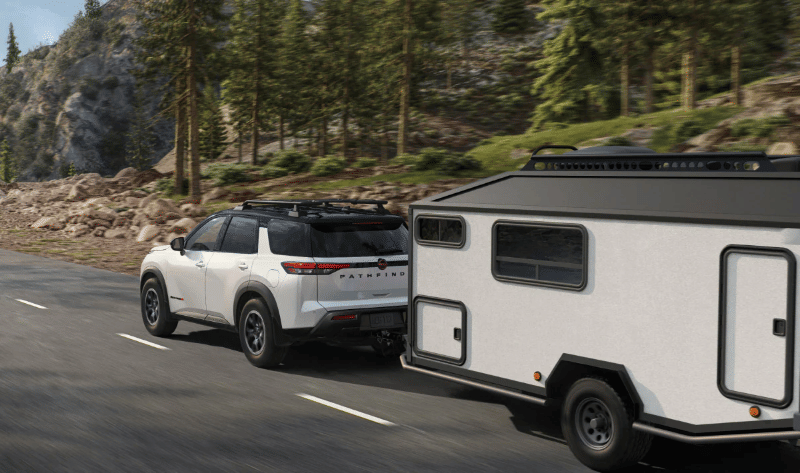 2026 Nissan Pathfinder towing a small enclosed trailer while driving on a highway.