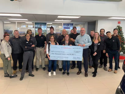 Un grupo de personas del concesionario presentando un gran cheque de donación a una organización benéfica local.