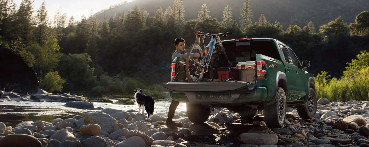 Una persona asegurando fácilmente una bicicleta de montaña en la caja de la Nissan Frontier 2026 utilizando el sistema de canales Utili-track® disponible.