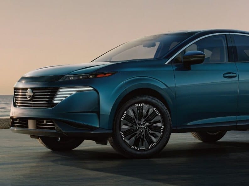 Un elegante Nissan Murano 2026 color verde azulado estacionado junto al océano al atardecer, mostrando su diseño moderno y parrilla frontal innovadora.
