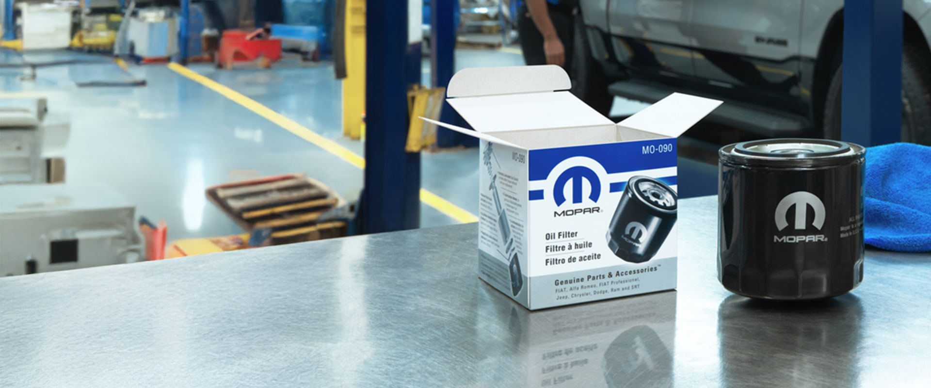 Un filtro de aceite Mopar y su caja están colocados sobre un banco de trabajo de acero inoxidable en un taller de servicio automotriz.