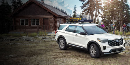 2025 Ford Explorer parked outside a rustic cabin as a family on bikes approaches.