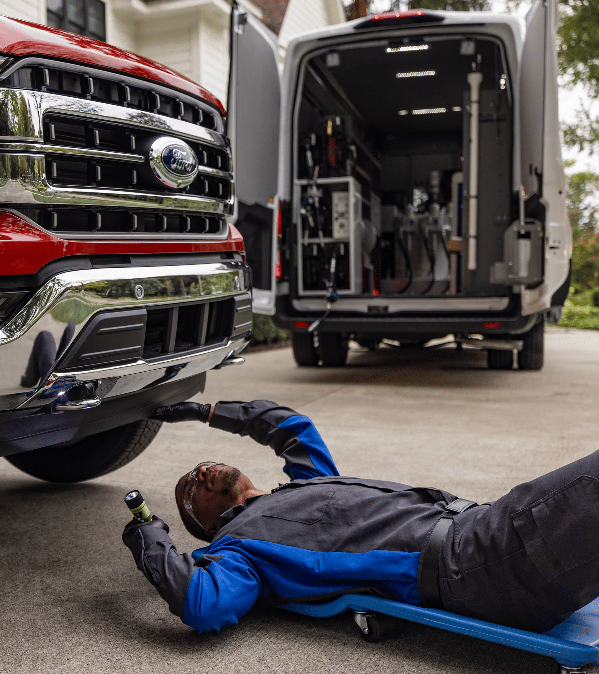 Un técnico de servicio de Ford trabaja en la entrada de una casa y se desliza bajo la parte delantera de una camioneta Ford F-150®