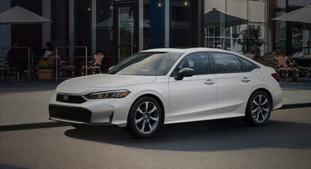 A white 2026 Civic Sedan parked in front of a row of restaurants with outdoor seating.