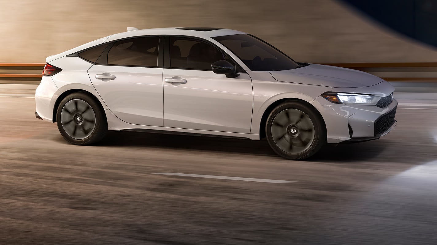 A 2026 Honda Civic Hatchback Hybrid with a modern design drives swiftly on a blurred urban road, conveying a sense of speed and sophistication.