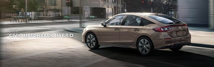 2026 Honda Civic Hatchback Hybrid in motion on an urban street, captured from the rear. Sleek design reflects the afternoon light, conveying modern efficiency.