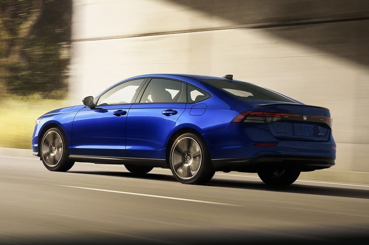 A sleek blue 2026 Honda Accord Hybrid drives under a bridge, its glossy finish catching light. The modern, aerodynamic design suggests speed and elegance.
