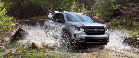 2026 Honda Ridgeline Sport in Solar Silver Metallic driving through water with dirt bikes in back.