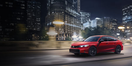 A red Civic driving through the city at night.