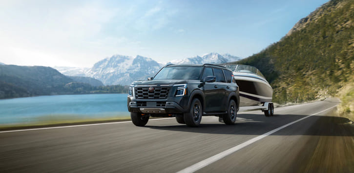 A black 2026 Armada driving along a mountain road with a boat on a trailer.