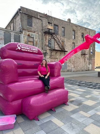 Woman sitting on a large, pink, inflatable chair for 'Making Strides Against Breast Cancer.'