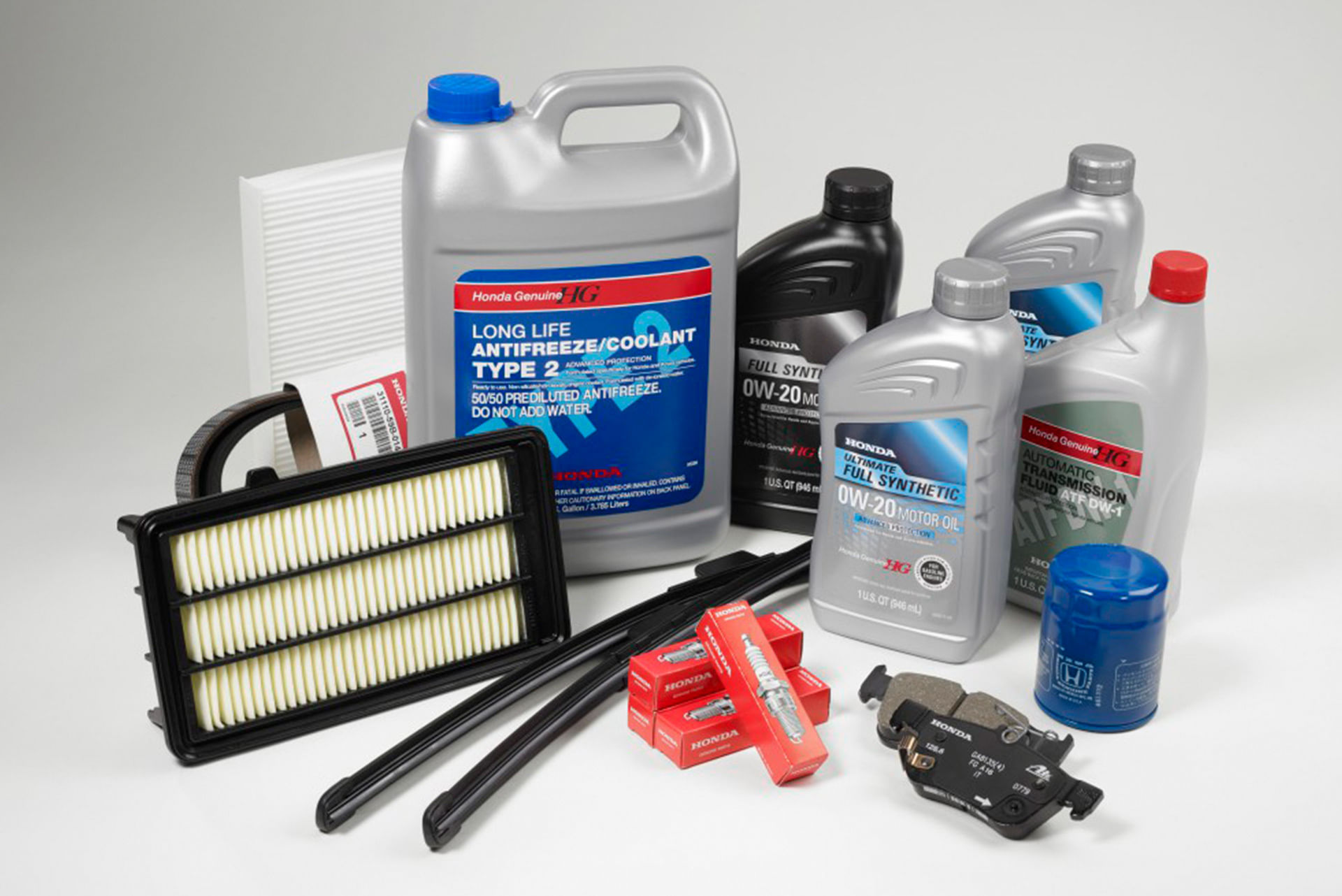 A collection of Honda Genuine Parts and Fluids, including motor oil, transmission fluid, coolant, an oil filter, air filters, wiper blades, spark plugs, and brake pads, all arranged on a white background.
