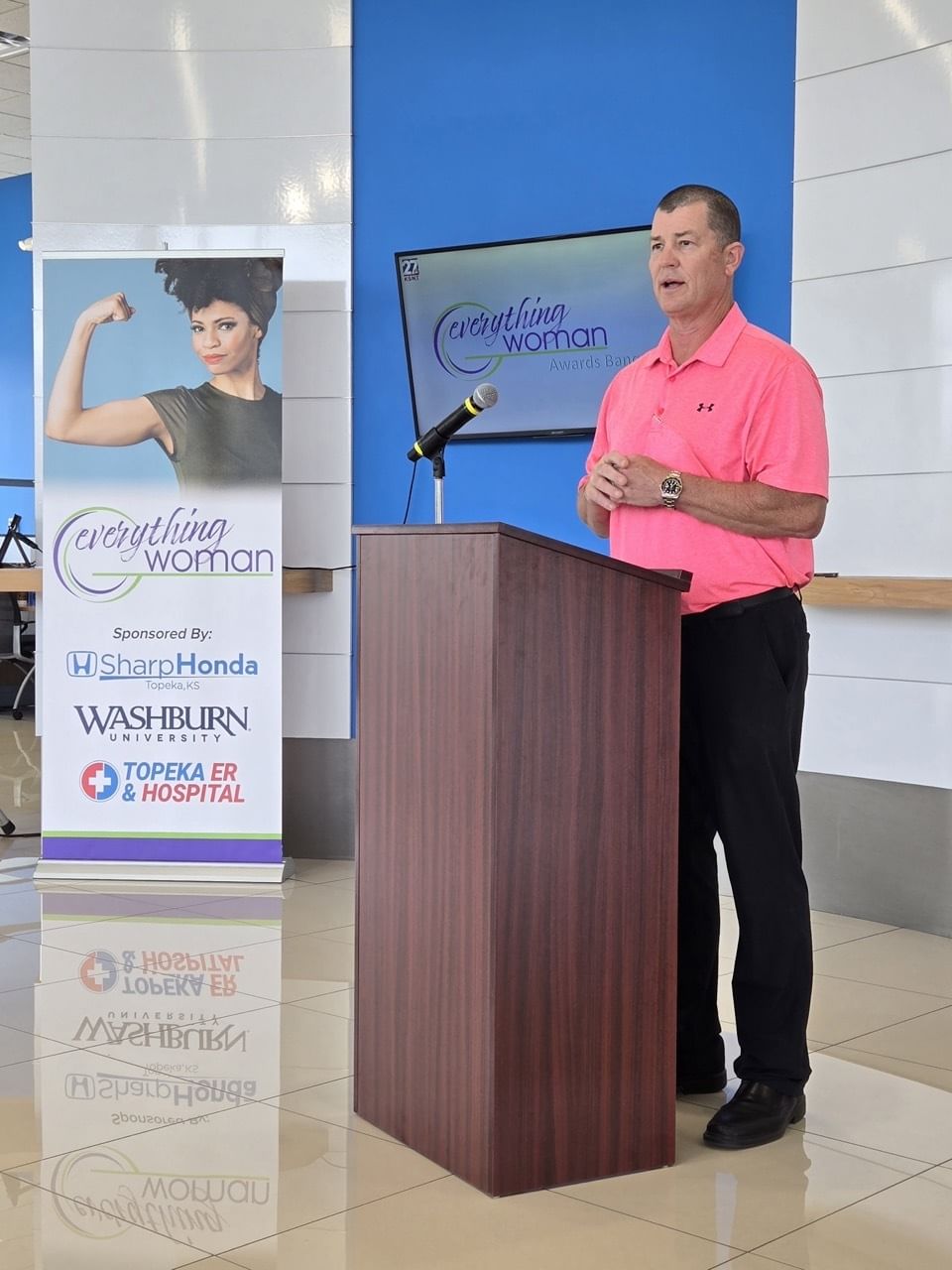 Man in pink polo speaks at 'Everything Woman' event podium