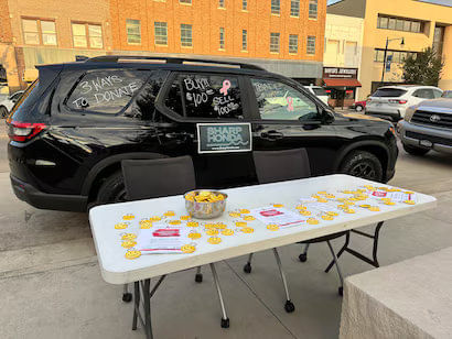 Black car with donation information in front of a table with breast cancer awareness items.
